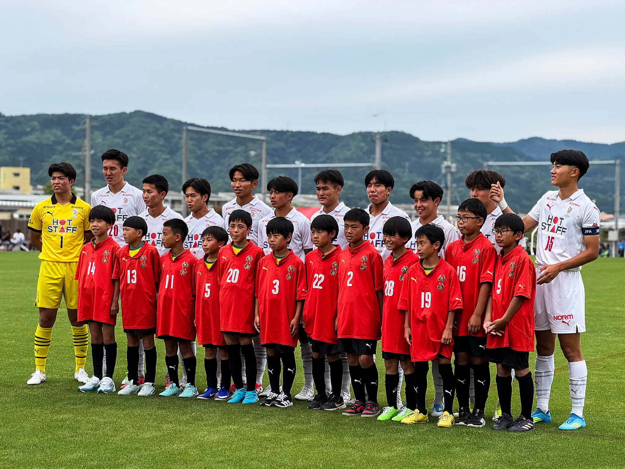 赤いユニフォームの子どもたちが神村学園の選手と並んで記念写真を撮っている