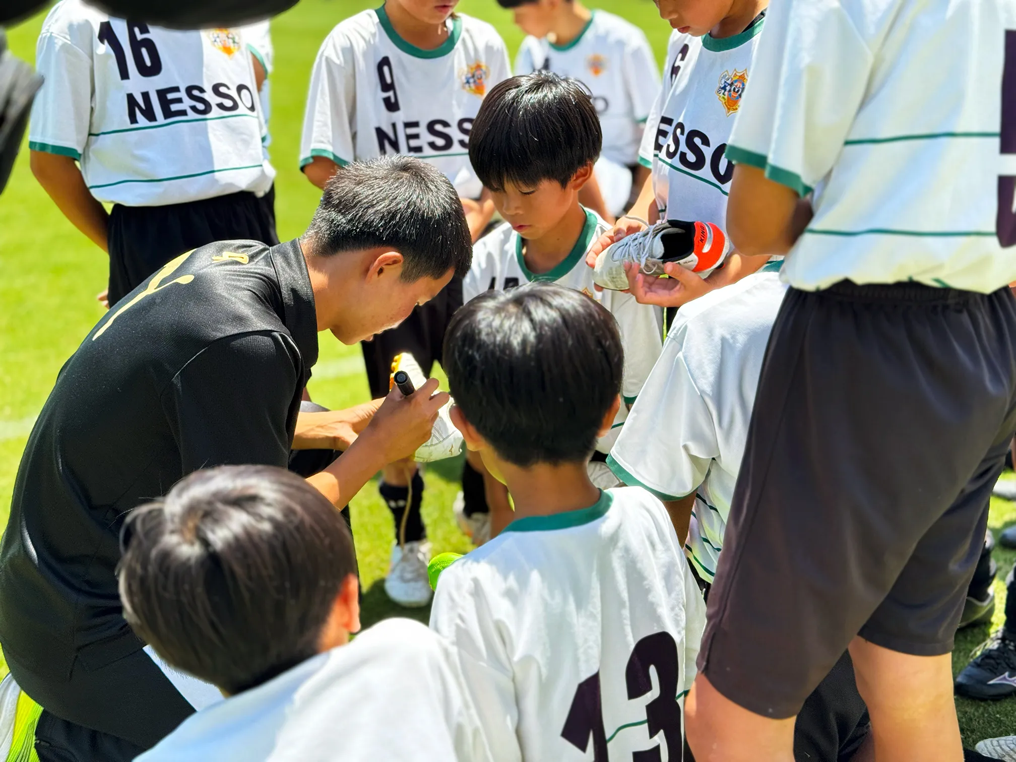 神村学園の選手がNESSO F.C.の子どもたちに囲まれてサインをしている様子