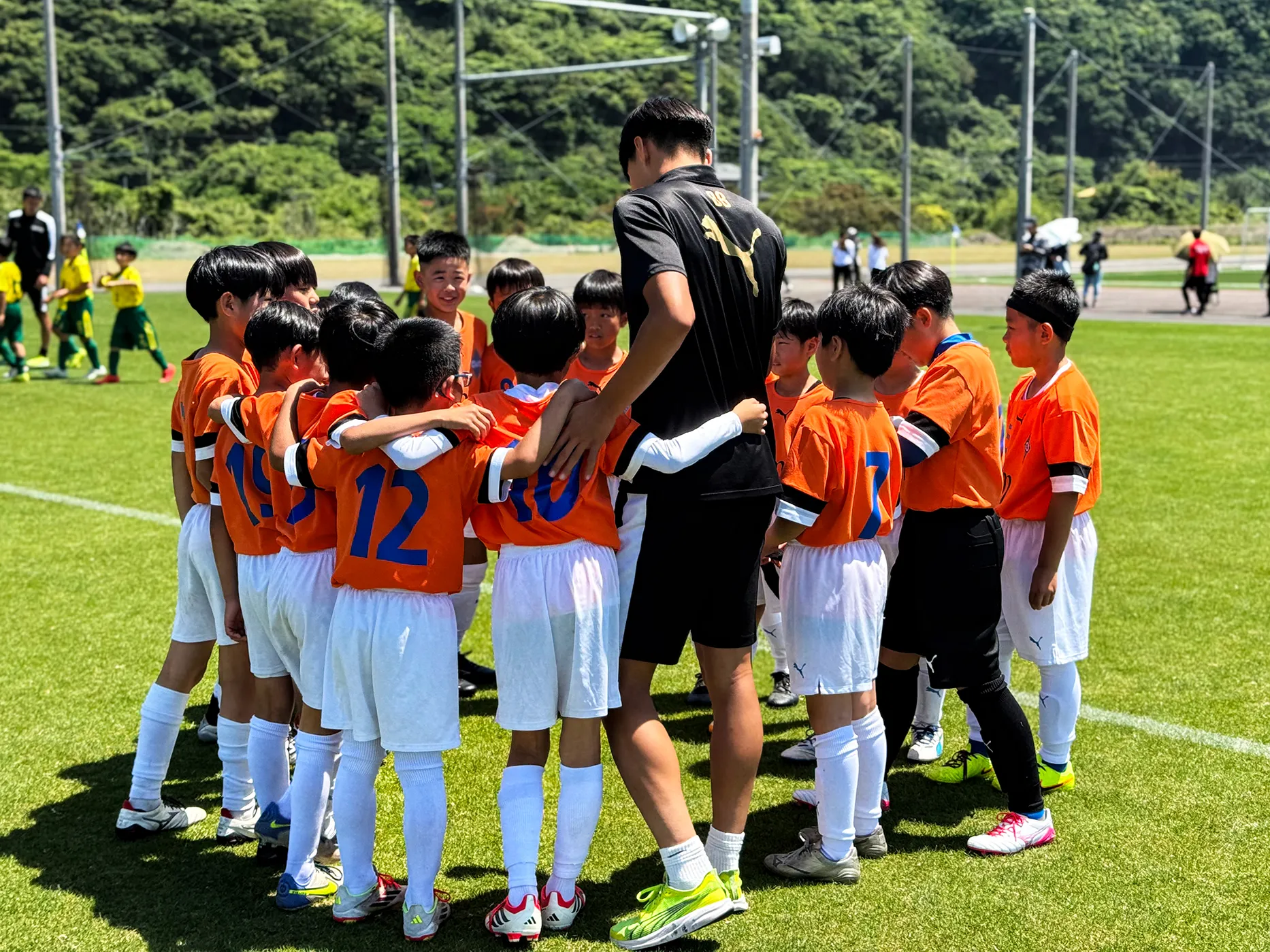 サッカー交流会のゲーム前、神村学園の選手を囲んで円陣を組む子どもたち