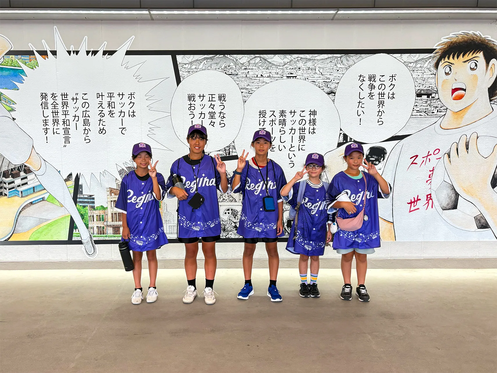 エディオンピースウイング広島の「キャプテン翼」壁画の前に並ぶ、レジーナのユニフォーム姿の子どもたち